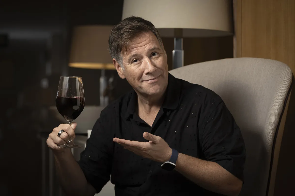 Carlos Latre sostiene una copa de vino tinto con gesto simpático, durante la presentación de los Premis Vinari 2025