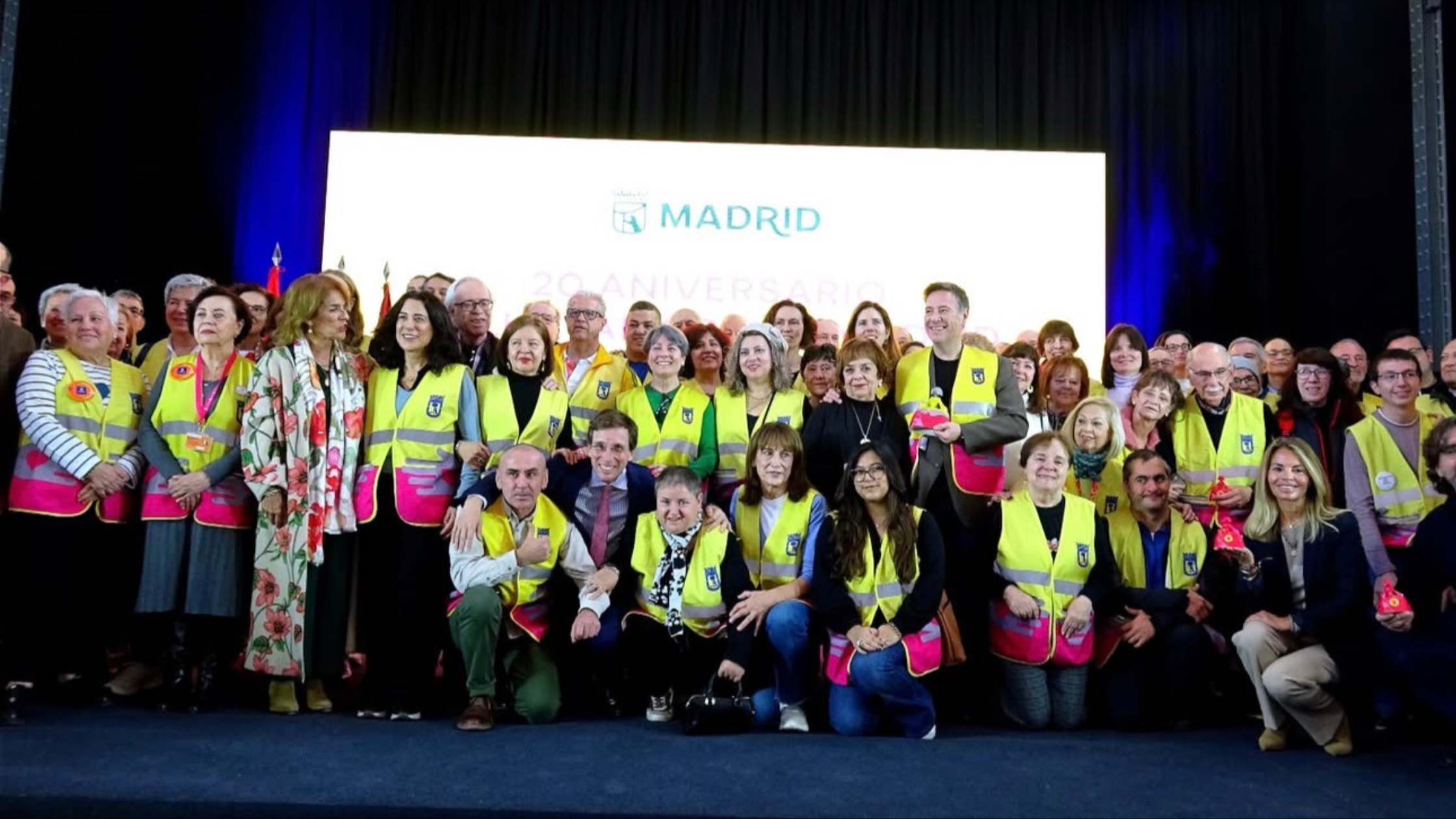 Carlos Latre junto a cientos de voluntarios por Madrid en el acto del 20º aniversario del programa municipal de voluntariado, donde fue nombrado Padrino de los Voluntarios por Madrid 2026. Foto de grupo con los voluntarios con chalecos amarillos y autoridades del Ayuntamiento.